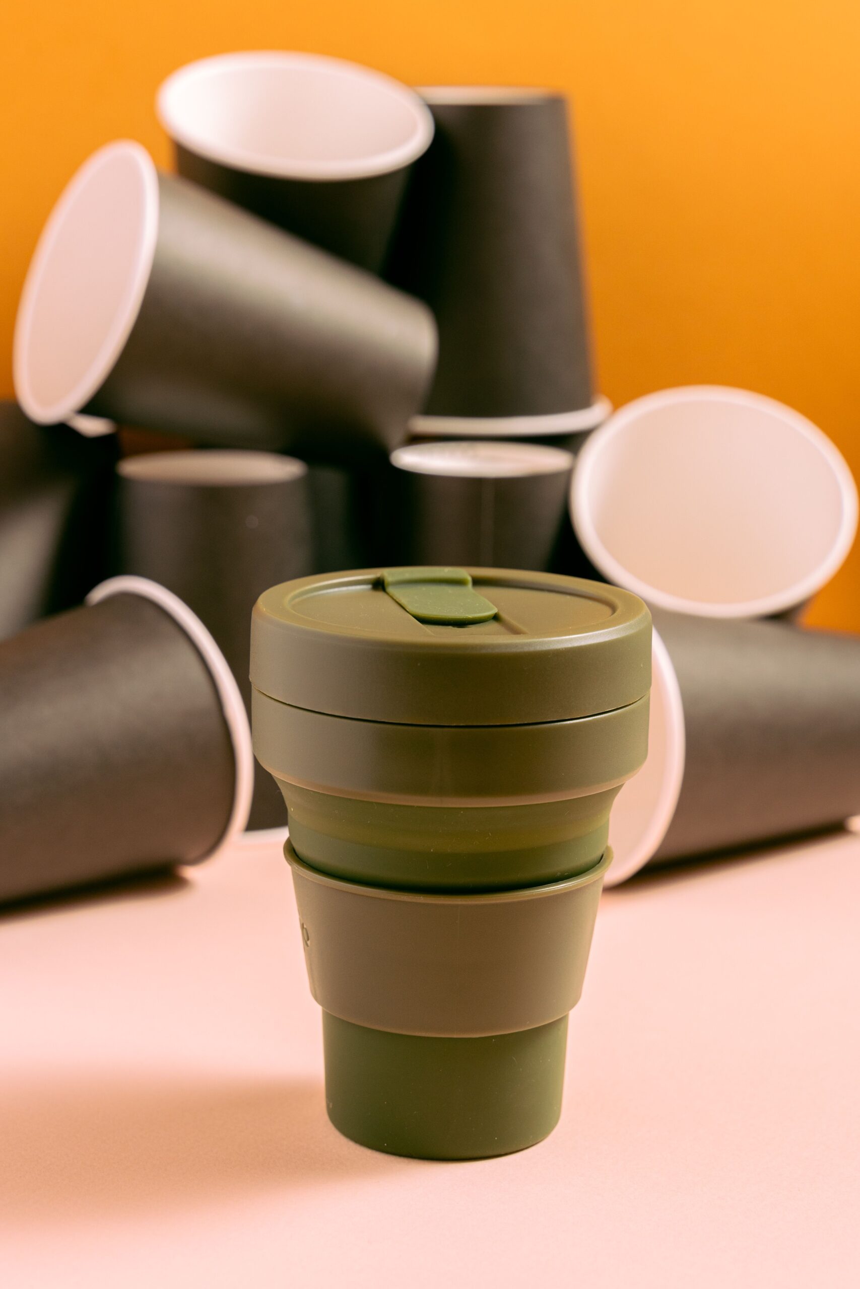 Collapsible reusable travel cup surrounded by disposable paper cups, highlighting an eco-friendly alternative.
